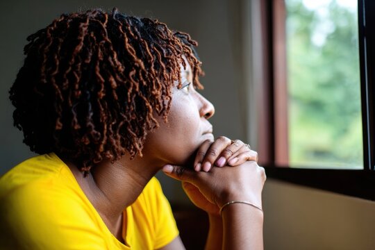 Woman with textured locs looking out a window in quiet thought, ideal for themes of hope, pause, and mindful reflection.