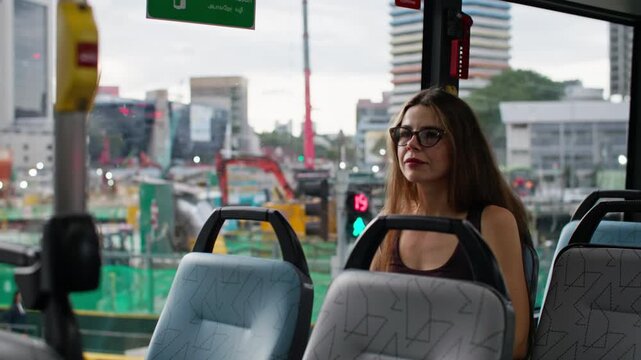 A woman sits on the seat of a city bus traveling through the streets of Singapore. A tourist looks out the window of public transport while traveling through Asia.