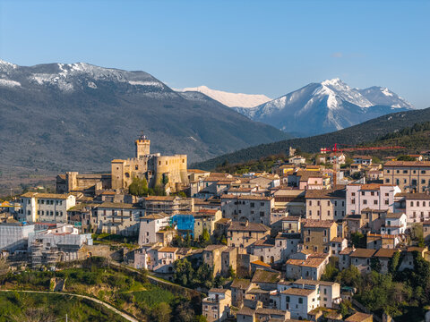 Aerial view of the historic Castello Piccolomini and stone houses of the village with snow-capped mountains in the background in Capestrano, Abruzzo, Italy.