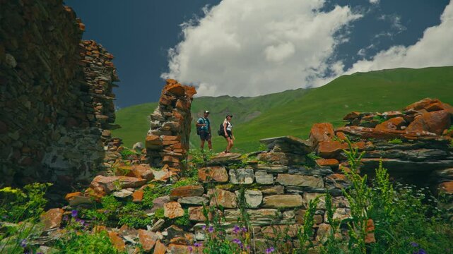 Couple explore fortress ruins in Truso Valley, Georgia, surrounded by green mountains and blue sky, capturing adventure, history, and scenic natural beauty.