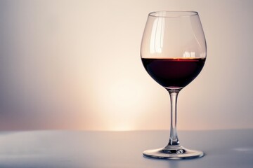 Fototapeta premium Elegant glass of red wine sits on a table, reflecting the warm glow of a setting sun, creating a tranquil and inviting atmosphere