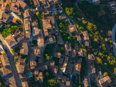 Aerial view of historic stone buildings and tiled rooftops of a traditional village surrounded by lush greenery and trees in golden hour light Capestrano, Abruzzo, Italy.