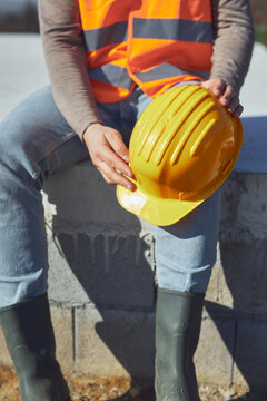 Construction worker working outdoors on a construction site, making a pause and holding a yellow hardhat.