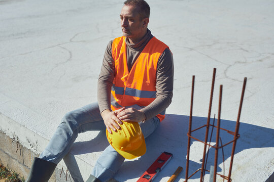 Construction worker working outdoors on a construction site, making a pause and holding a yellow hardhat.