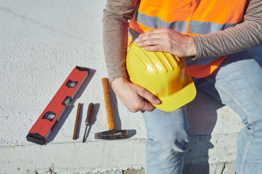 Construction worker working outdoors on a construction site, making a pause and holding a yellow hardhat.