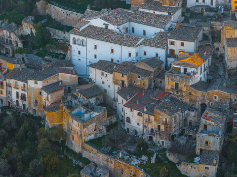 Aerial view of the historic stone houses and tiled rooftops of the medieval village with the white facade of the Piccolomini Castle in Capestrano, Abruzzo, Italy.