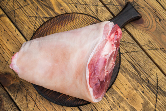 Uncooked pork shank hamhock showing skin texture fat layers and structural anatomy on wooden surface with herbs for technical food photography.