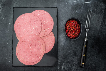 Naklejka premium Smooth pink salam beef slices placed on a black slate board with vintage fork and pepper perfect for charcuterie and gourmet recipe visuals