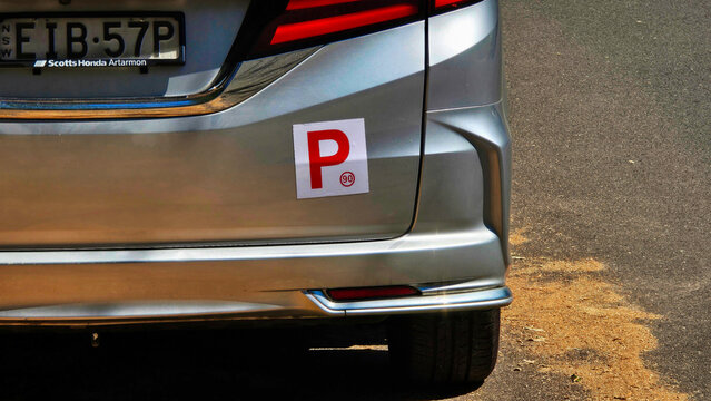 Car with learner driver sign parked on the street in a sunny location. P Sign of learner Australia.White P 90 Plate sign at the back of a car showing that a probationary driver is behind the wheel