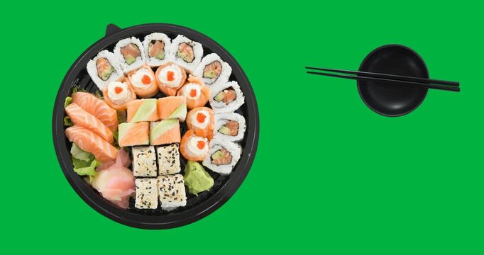 Overhead view of sushi in a round plate , bowl and chopsticks on black surface
