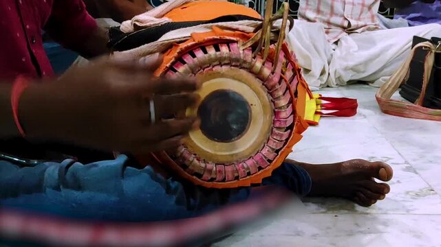 Close-up of a musician playing a traditional Indian hand drum, likely a khol-mridanga, at a cultural devotional gathering. Highlighting percussion instruments and rhythmic performance in Kirtan song.