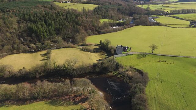 The River Esk winds through green fields and dense trees in the Scottish Borders. This scene shows a clear view of the landscape near Langholm on the A7. Hills rise in the background