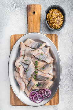 Marinated salted herring fish pieces with mustard and thyme in white plate. Nordic preserved seafood top view with copy space.