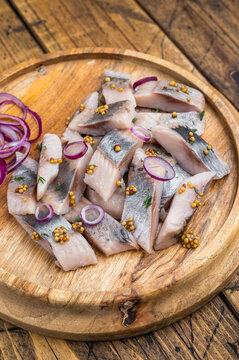 Pickled herring chunks cured in salt and brine served with onion and mustard. Traditional seafood appetizer on rustic wood.