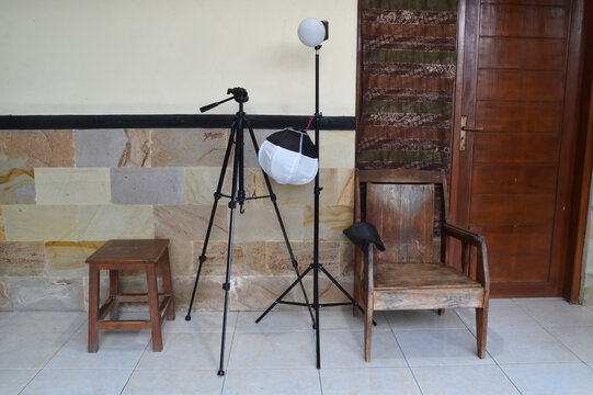 A top-down centered shot featuring a black photography softbox and tripod standing beside a classic wood table and chair set on a residential tiled patio.