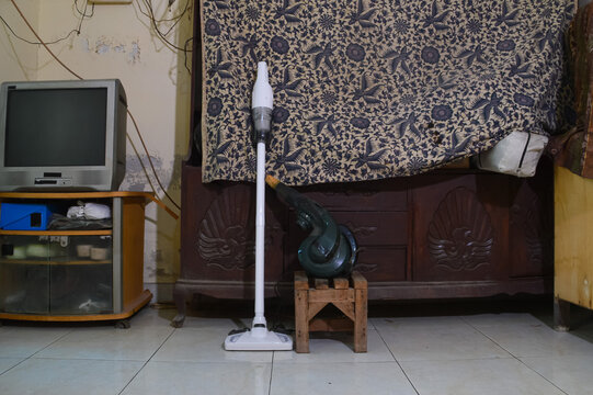 A front eye-level view of a portable cordless vacuum cleaner and an electric blower tool placed on a tiled floor inside a home living room for cleaning.