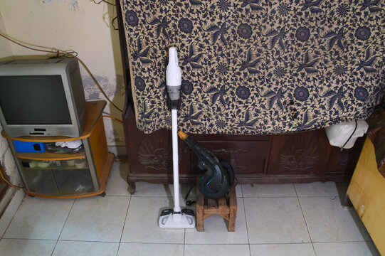 A top-down centered shot looking at a wireless vacuum cleaner and electric blower situated on a tiled living room floor, ready for deep cleaning tasks.