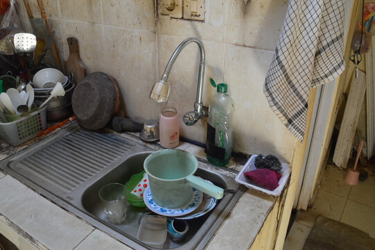 A quarter right elevated shot looking down at a kitchen sink containing used plates and a blue water dipper under a flexible silver swan neck water tap.