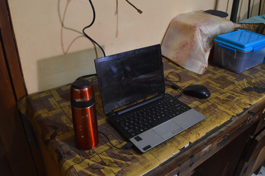 A quarter left high angle view of a silver laptop accompanied by an external mouse and a mini vacuum flask, positioned on a wooden table for a productive study session.