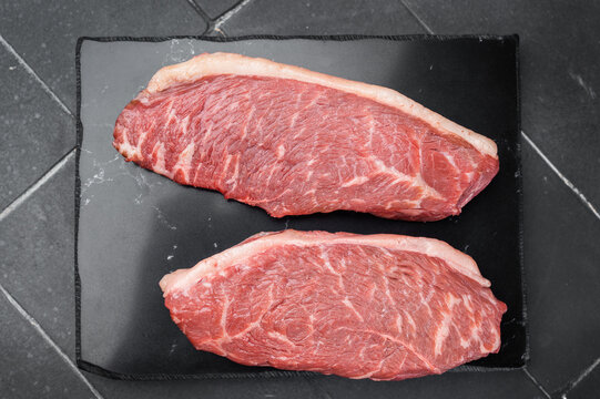 Raw top sirloin cap beef steaks also known as rump cap with rosemary on slate board, dark stone background