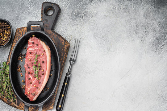 Raw picanha beef steak also known as top sirloin cap and rump cap with thyme and pepper in cast iron pan, stone background