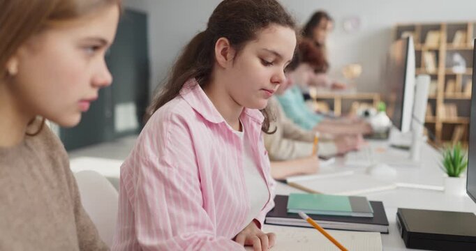 Students teenagers girls studying in classroom with computers. They take notes and finish tasks. Teacher supports learning in school. Clear concept of digital education for students.