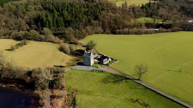 The River Esk winds through green fields and dense trees in the Scottish Borders. This scene shows a clear view of the landscape near Langholm on the A7. Hills rise in the backgro
