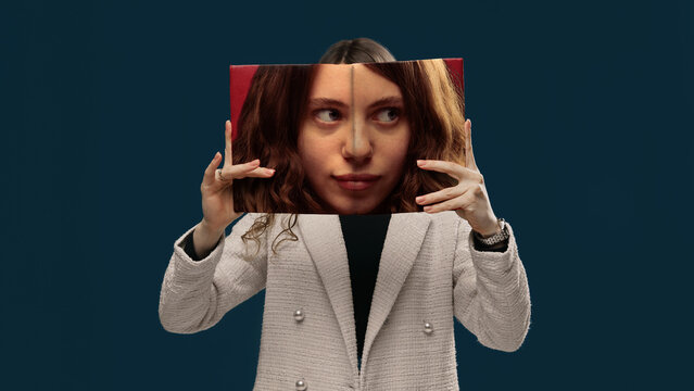 Young woman holding printed face panel aligning with real face studio portrait. Concept of dual personality, self image, perception gap, authenticity and social identity construction.