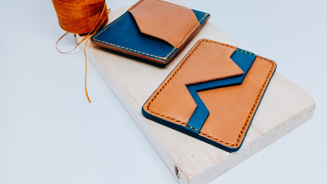 Handcrafted leather card holder wallets in tan and blue color on a wooden board with thread roll.