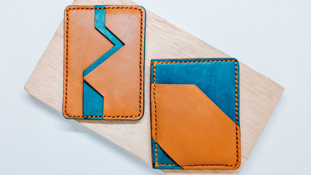 Pair of handmade leather card holder wallets with unique geometric design on wooden board.