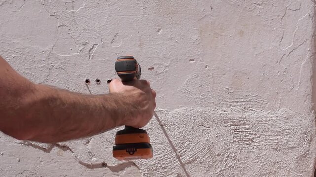 A Hispanic man drilling a hole in a white wall with a cordless drill, seen from behind