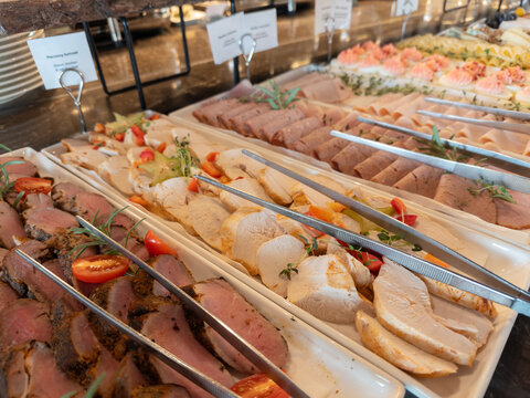 Sliced roast chicken, various cold cuts, and fresh salads displayed on a self-service buffet line, offering diverse culinary options for a rich meal experience