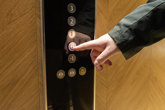 Human hand presses the illuminated ground floor zero button on a sleek elevator panel, symbolizing travel decisions and urban destination choices