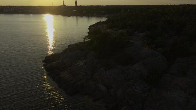 Aerial view tilting over rocky cliffs, revealing the cityscape of Hanko, sunset.