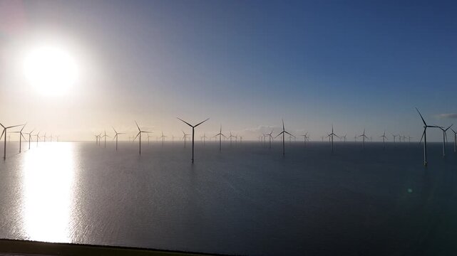 Crisp aerial perspective over the dyke and sea with dramatic light across the offshore turbines.