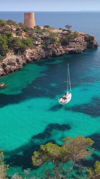 Aerial vertical shot of a sailboat anchored in the turquoise waters of Cala Pi, Mallorca. iconic Spanish coastline in the Balearic Islands, Cala Pi, Mallorca