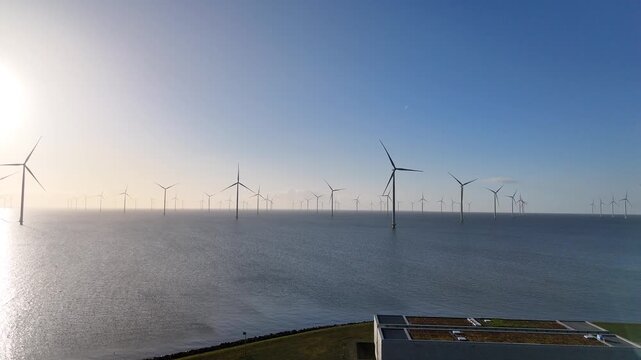 Drone descends beside a modern metal clad building on Breezanddijk with offshore wind turbines visible behind it.