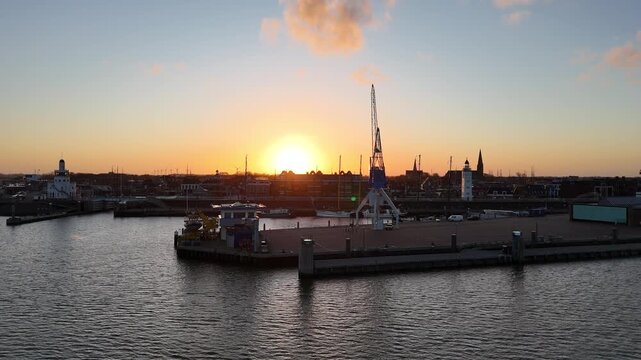 Slow drone push toward the harbor crane framed against the glowing morning sun.