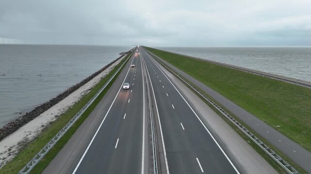 Drone ascends slowly from the median and reveals the immense length of the Afsluitdijk stretching toward distant land.