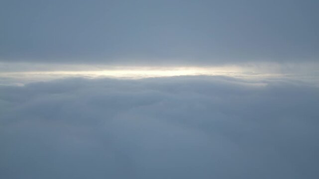 Aerial View Above Thick Clouds with Sun Peeking Through Horizon