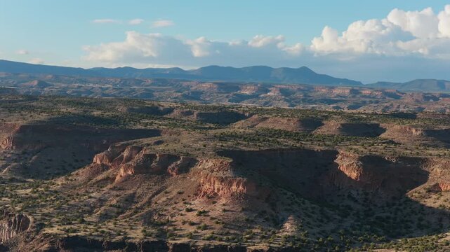 A high altitude drone vista of southwest mesa canyons and mountains. Scenic cloud formations and warm light illuminate the vast, universal high desert terrain for cinematic b-roll.