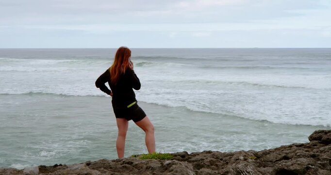 Solitude by the Shore: A woman, standing on the edge of the rocky shore, finds solace gazing at the vast ocean. A serene scene of self-reflection. 