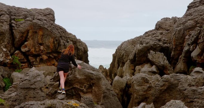 Woman Climbing Rocky Terrain: A solitary figure, a woman fearlessly navigates the rugged, uneven landscape of weathered stone, finding strength in the pursuit of overcoming challenges.