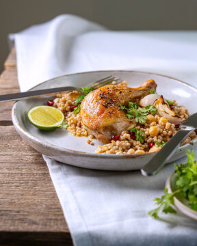 Roasted chicken leg with pearl couscous, chickpeas and lime served on rustic ceramic plate