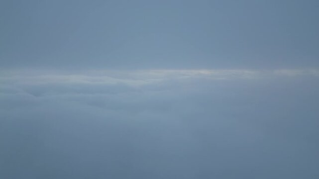Aerial View Above Thick Clouds with Sun Peeking Through Horizon