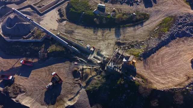 A bustling construction site reveals machinery at work reshaping the land under clear skies. Heavy equipment, trucks, and scattered materials create a vivid scene of industry and progress.
