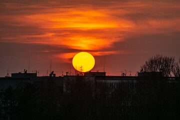 Obraz premium Large sun setting over city skyline with dramatic orange sky and silhouettes of buildings