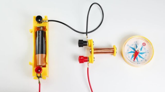 A hand connects wires to a battery and coil showing electromagnetism with compass needle deflection educational motion clip.