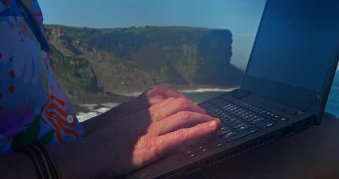 Laptop Amidst the Horizon: A person is immersed in their work, fingers dancing across the keys of a laptop, overlooking a breathtaking coastal cliffside view.
