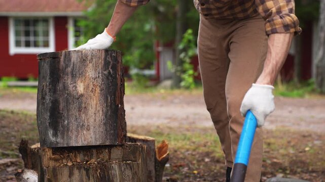 Close up of an axe stuck in a large log. Young man struggling to split wood in the countryside. Concept of persistence and hard work.